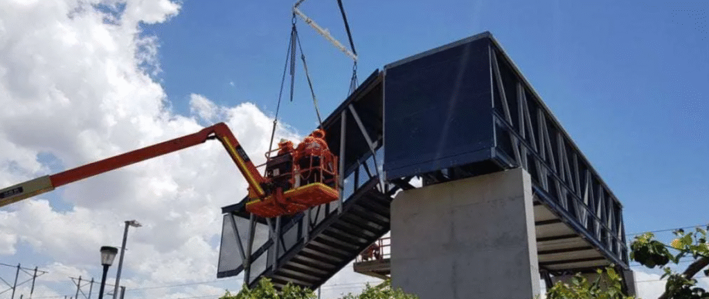Workers installing a lightweight FRP pedestrian bridge structure using a crane and lift.